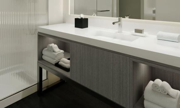 A section of a guest bath at AC Hotel St. Augustine shows warm grey and white tones a sink and walk in shower