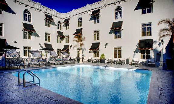 The Casa Monica Hotel's outdoor pool on a sunny day, surrounded by comfortable striped cabanas and beach chairs.
