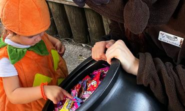 A child in a pumpkin costume chooses a candy from a large black bowl