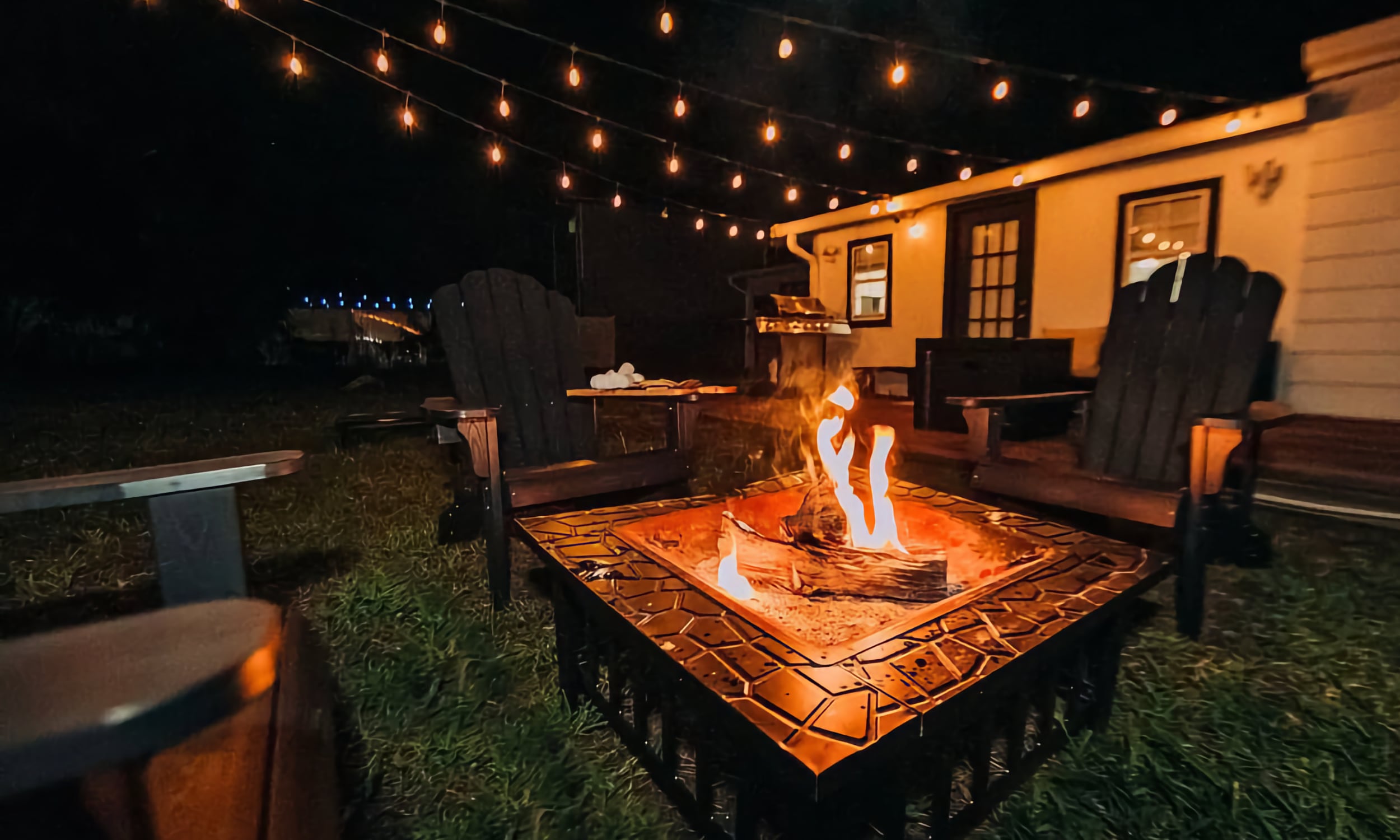 A back yard lit by strings of white lights and a fire pit