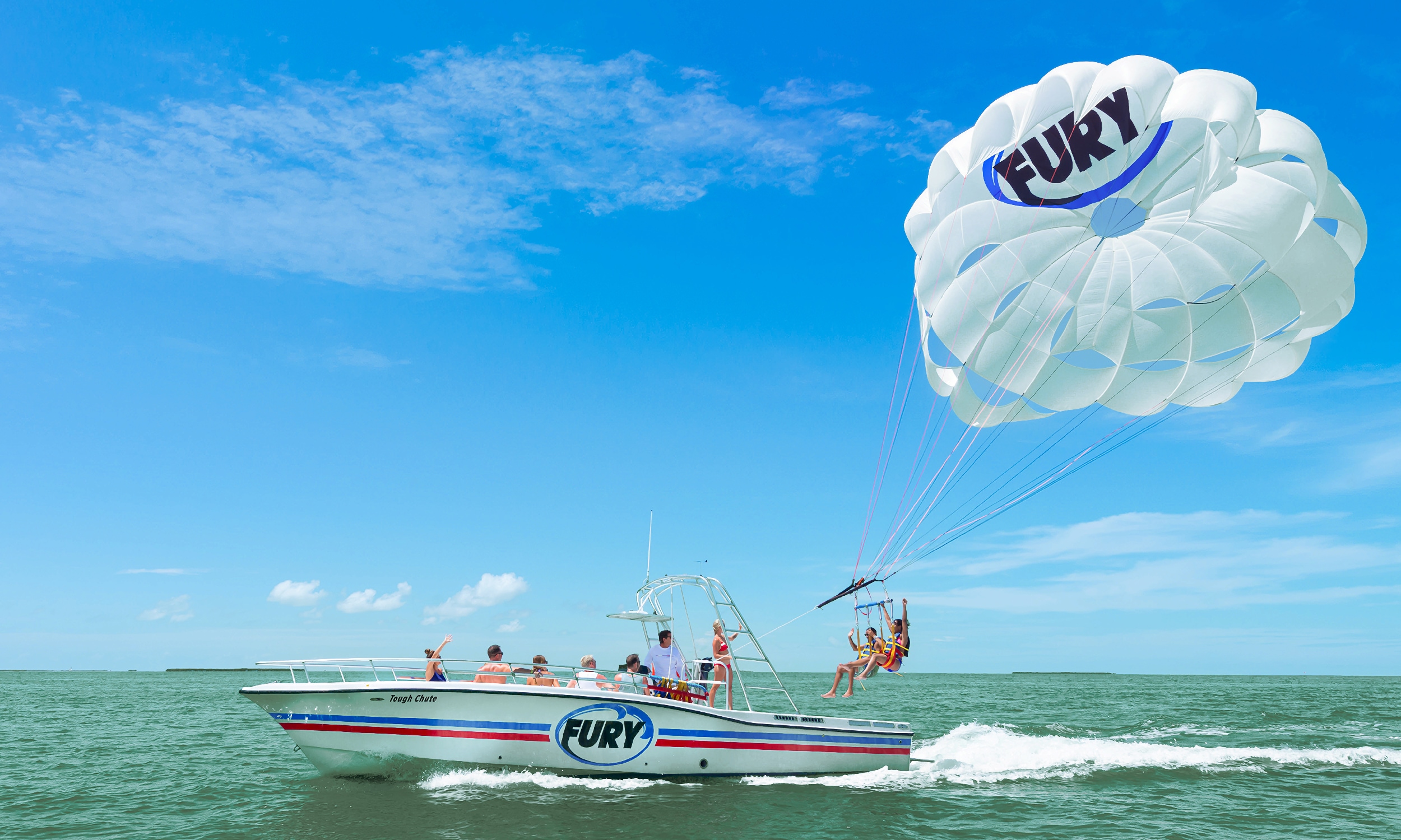 A fast parasail boat, moving along in the open ocean as two peole hang from the sail
