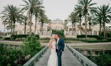 A bridal couple kisses on a wooden bridge in front of the clubhouse at Hammock Beach Golf Resort and Spa
