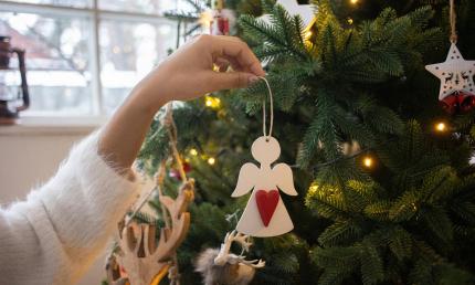 A woman hangs a white angel on a tree decorated in gold and white ornaments