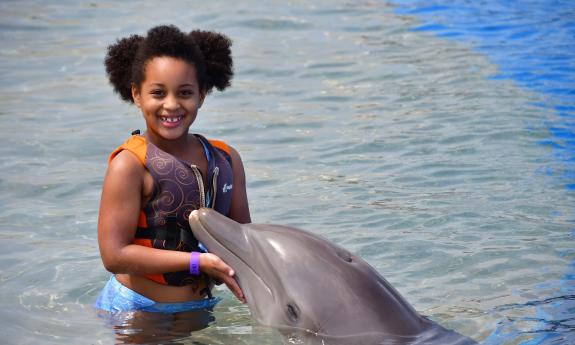 A young girl stands in a salt-water pool with a dolphin