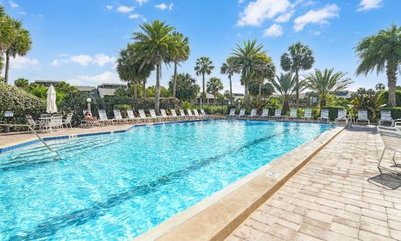 This pool with ample seating is surrounded by palm trees and landscaped lawn