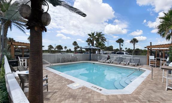 The pool with stone patio, seating, and a fence at an hotel between the ocean and the marsh