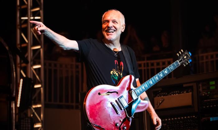 Peter Frampton laughs and points at his audience while performing on stage.