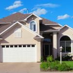 A full color image of a house in the suburbs. It is beige and has a manicured lawn.